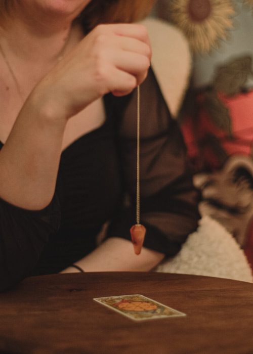 Marina håller en pendel i sin högra som rör sig över ett tarotkort under en medial vägledning. mediala tjänster.